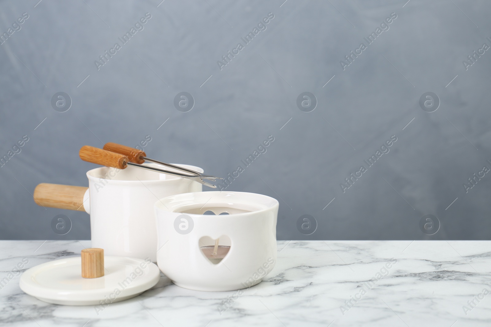 Photo of Fondue set on white marble table against light grey background, space for text