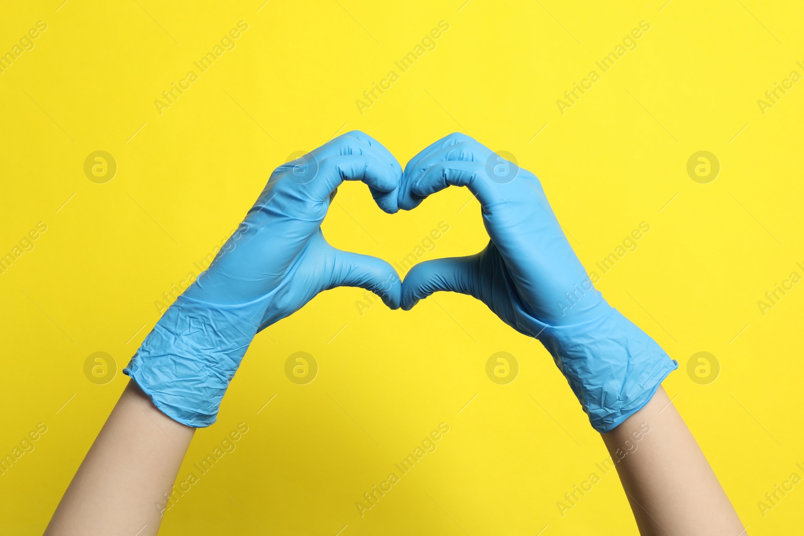 Photo of Doctor in medical gloves making heart with hands on yellow background, closeup