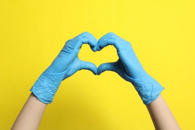 Doctor in medical gloves making heart with hands on yellow background, closeup