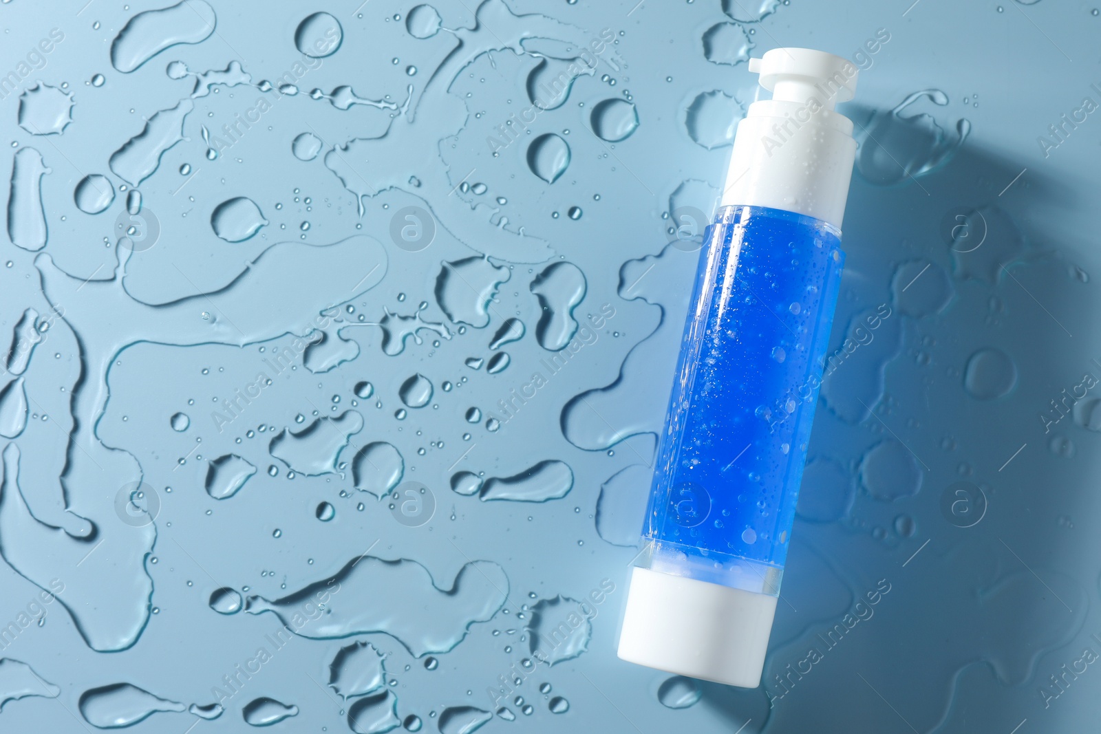 Photo of Bottle of cosmetic product and water drops on light blue background, top view. Space for text