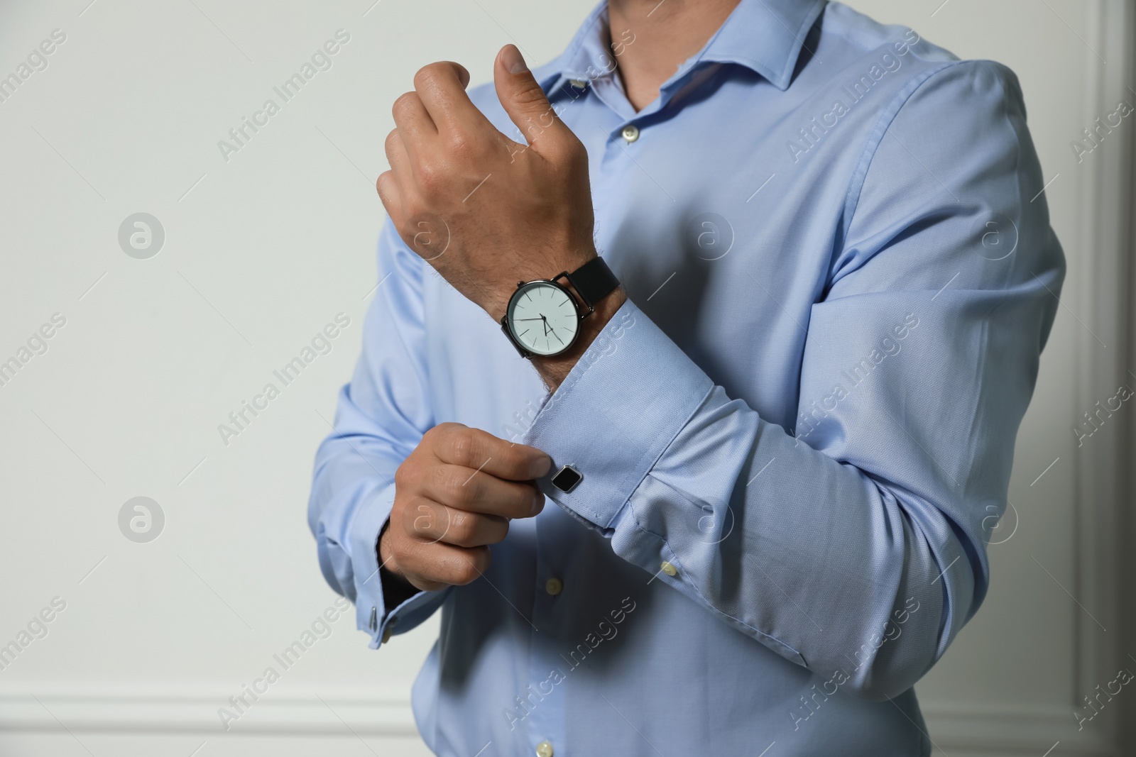 Photo of Stylish man putting on cufflink against grey wall, closeup