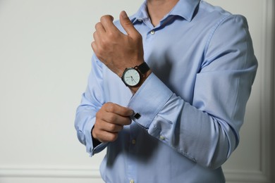 Photo of Stylish man putting on cufflink against grey wall, closeup