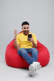 Emotional young man using smartphone on bean bag chair against grey background