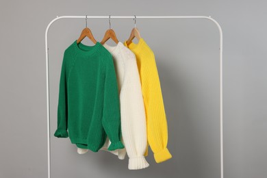 Photo of Rack with different warm sweaters on light grey background