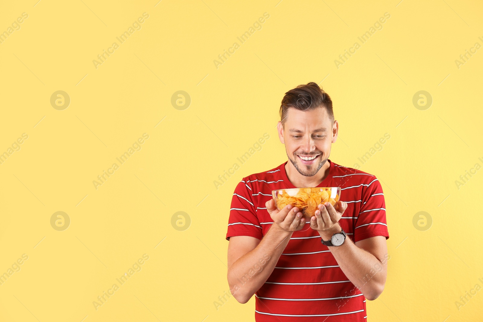 Photo of Man with bowl of potato chips on color background. Space for text