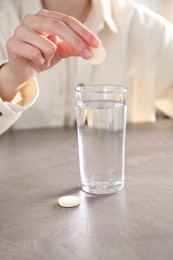 Woman putting effervescent pill into glass of water at grey table, closeup