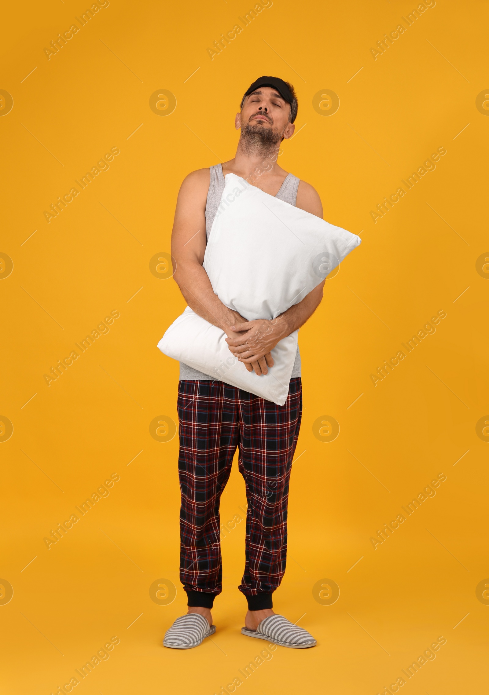 Photo of Man with pillow and eye mask in sleepwalking state on yellow background