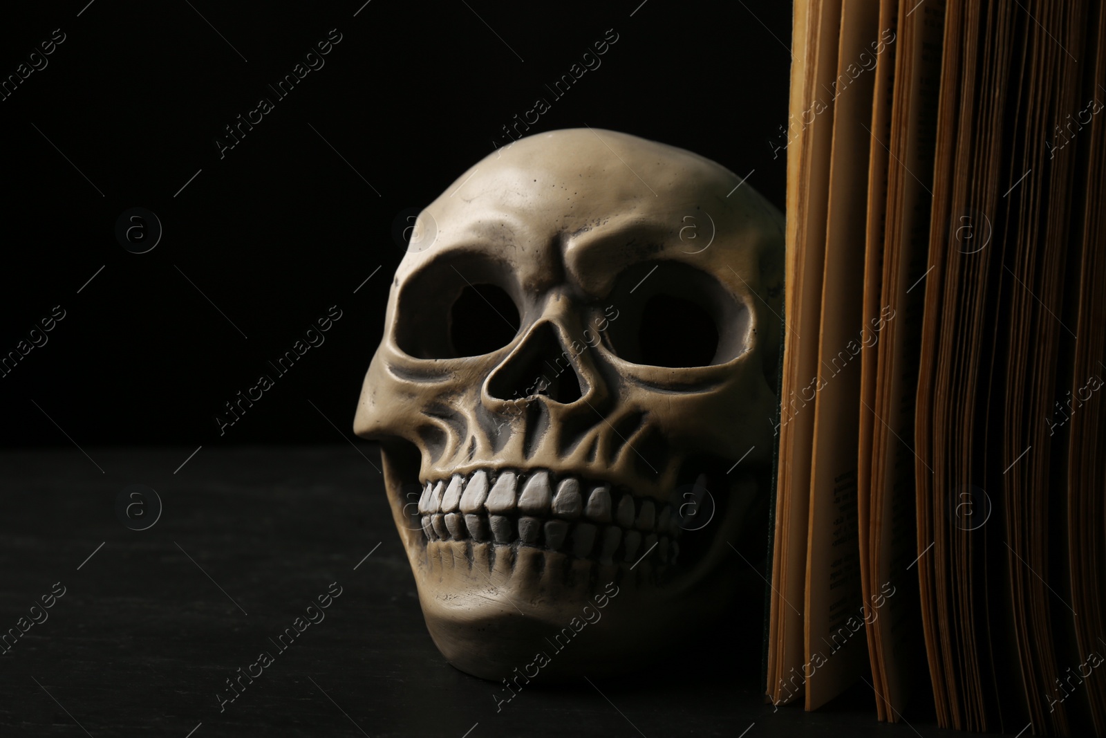 Photo of Human skull and old book on black table, closeup. Space for text