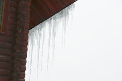 House with icicles on roof, space for text. Winter season