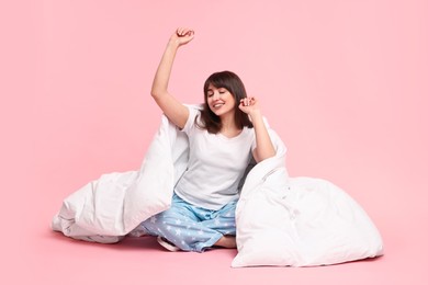 Happy woman in pyjama wrapped in blanket on pink background