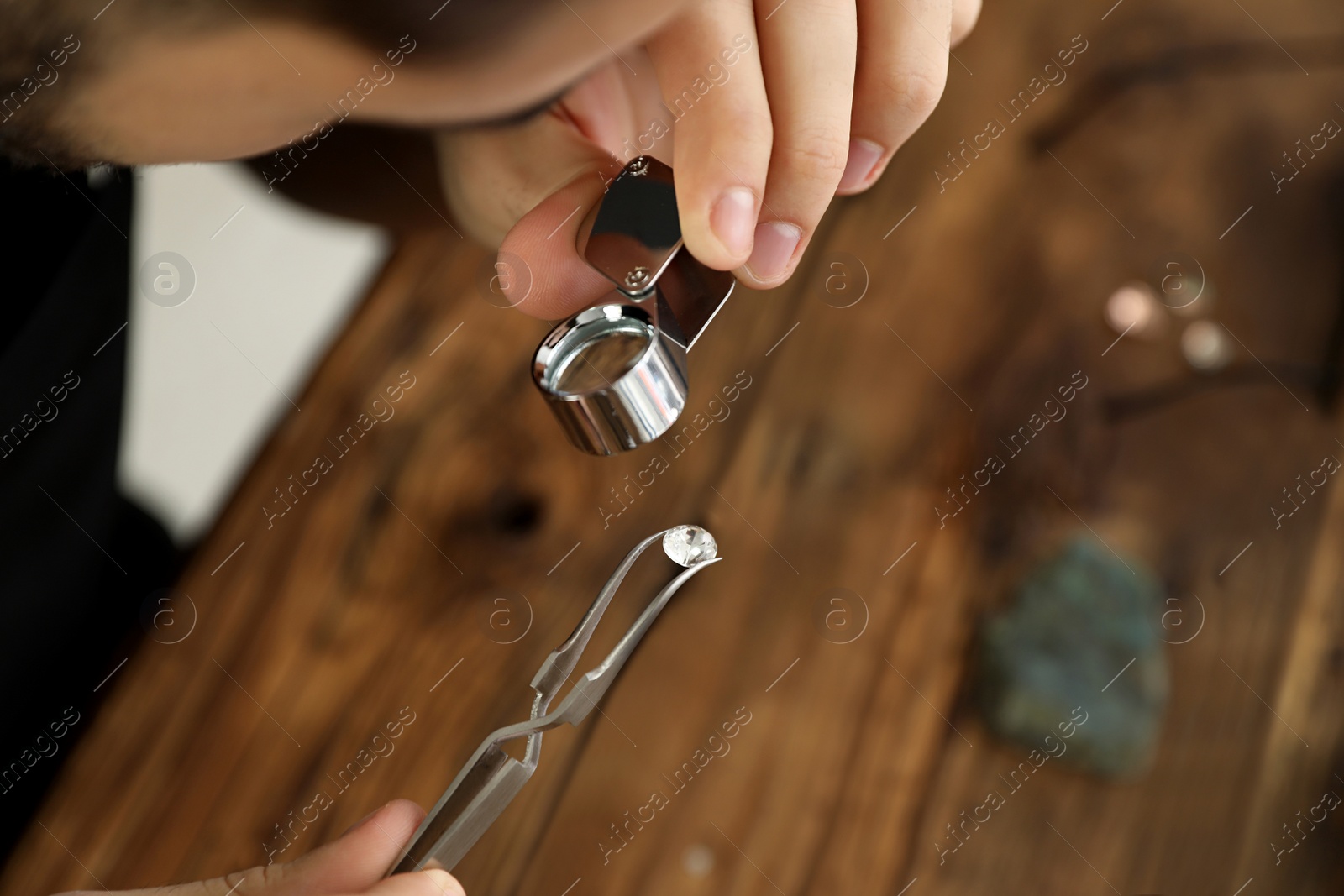 Photo of Male jeweler evaluating precious gemstone at table in workshop, closeup