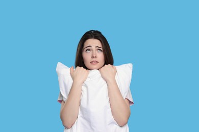Photo of Unhappy young woman with pillow on light blue background. Insomnia problem