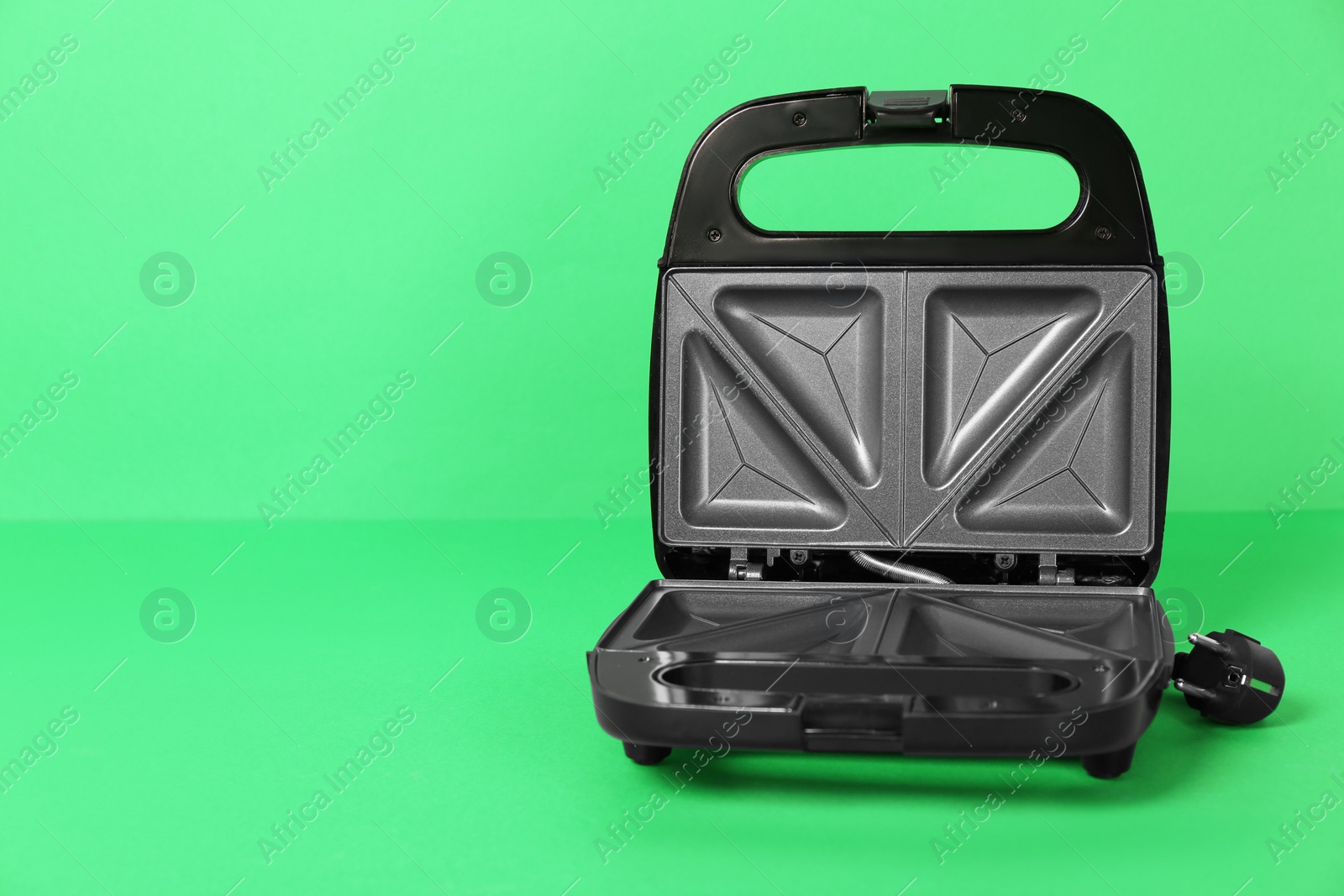 Photo of Open electric sandwich maker on green background, space for text