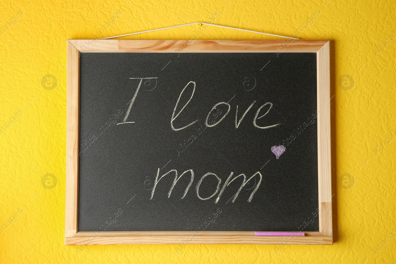 Photo of Chalkboard with phrase I LOVE MOM hanging on yellow wall