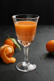 Photo of Tasty tangerine liqueur in glass and fresh fruits on black textured table