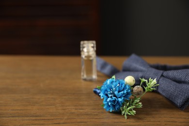Photo of Wedding stuff. Stylish boutonniere, bow tie and perfume bottle on wooden table, closeup. Space for text