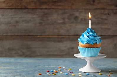 Photo of Delicious birthday cupcake with candle on table