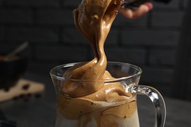 Photo of Pouring cream for dalgona coffee into glass mug on dark background, closeup