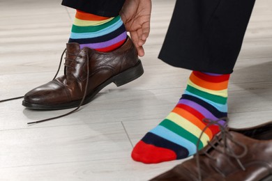 Photo of Man with colorful socks putting on stylish shoes indoors, closeup