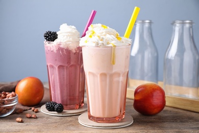 Photo of Tasty peach and blackberry milk shakes in glasses on wooden table