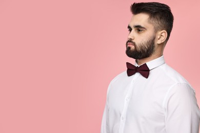 Portrait of handsome man in shirt and bow tie on pink background. Space for text