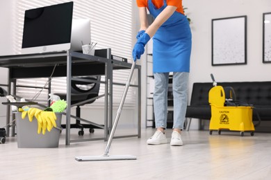 Photo of Cleaning service worker washing floor with mop, closeup. Bucket with supplies and wet floor sign in office