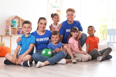 Happy volunteers with children sitting on floor indoors