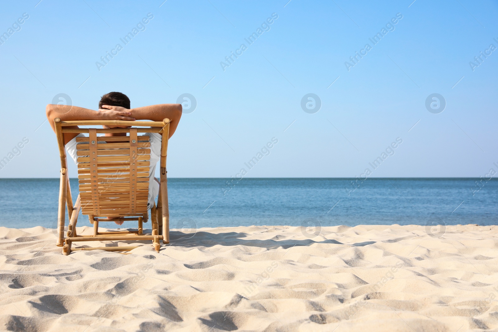 Photo of Young man relaxing in deck chair on sandy beach