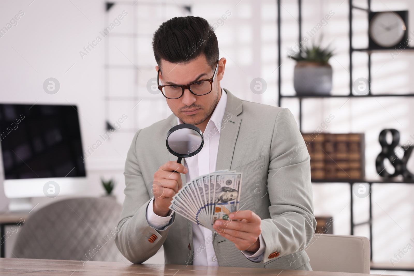 Photo of Expert authenticating 100 dollar banknotes with magnifying glass at table in office. Fake money concept