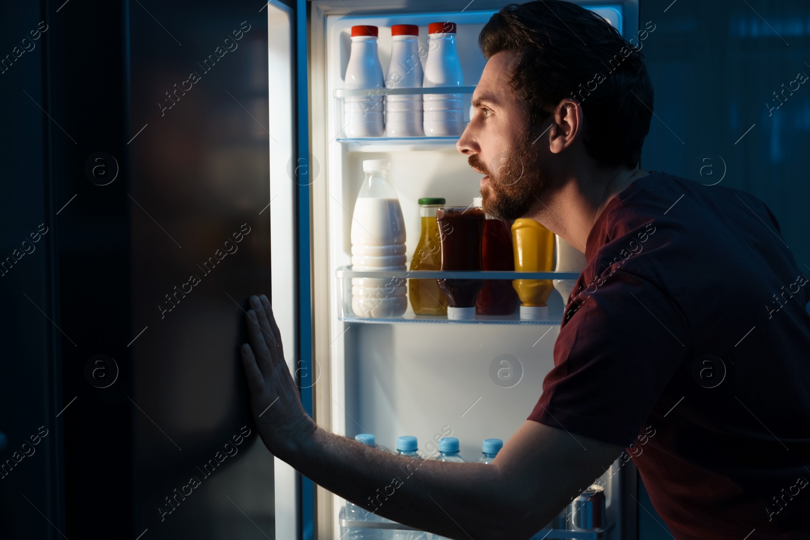 Photo of Man choosing food from refrigerator in kitchen at night. Bad habit