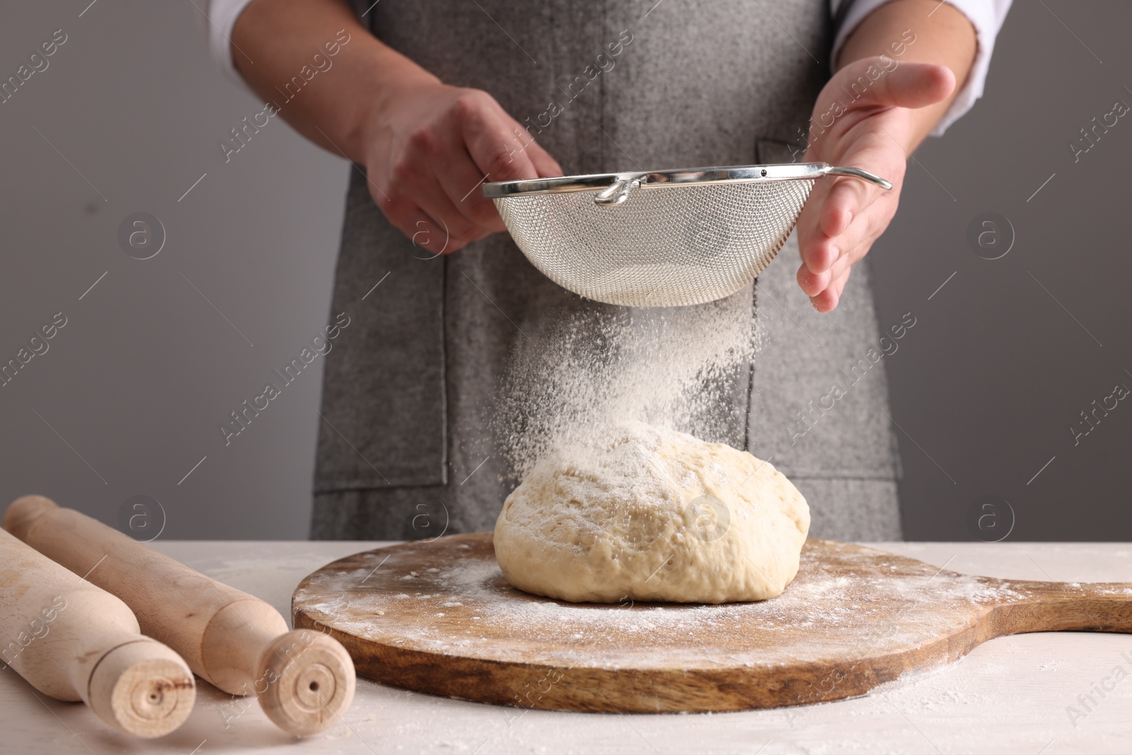 Photo of Man sprinkling flour over dough at table near grey wall, closeup