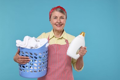 Photo of Happy housewife with detergent and basket full of laundry on light blue background