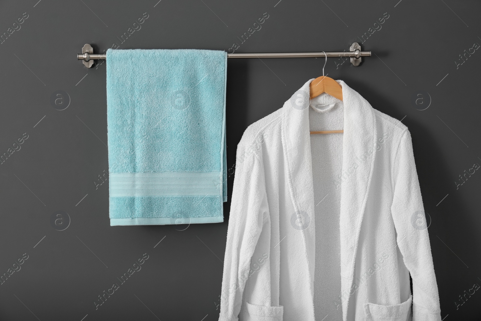 Photo of Hanger with clean towel and bathrobe on grey wall