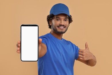 Image of Happy courier holding smartphone with empty screen and showing thumbs up on beige background