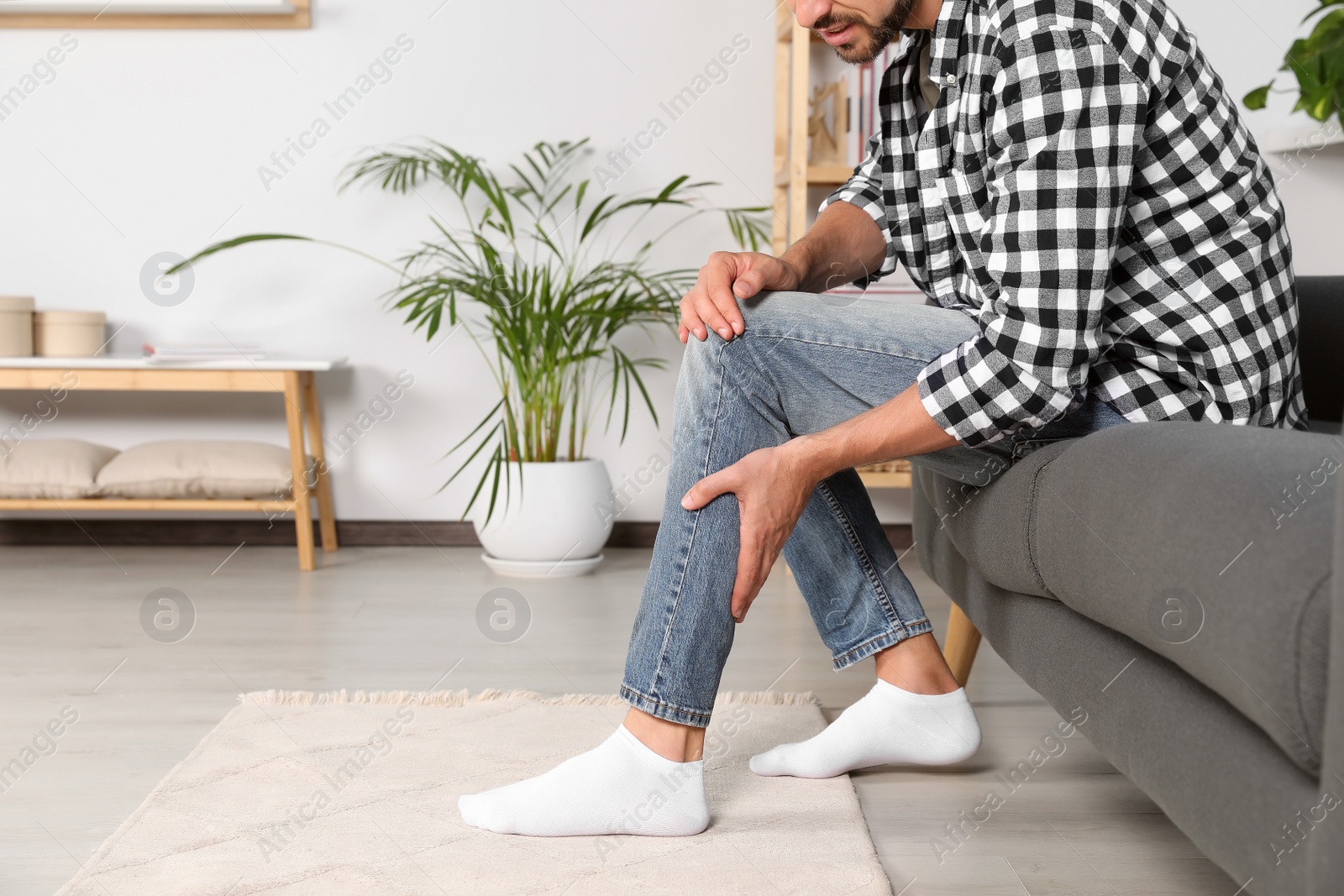 Photo of Man suffering from pain in leg on sofa at home, closeup. Space for text