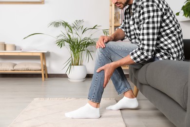 Photo of Man suffering from pain in leg on sofa at home, closeup. Space for text