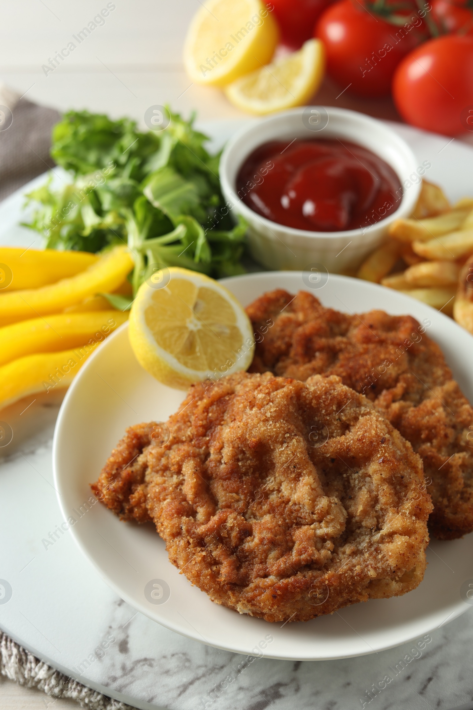 Photo of Tasty schnitzels served with potato fries, ketchup and vegetables on marble board, closeup