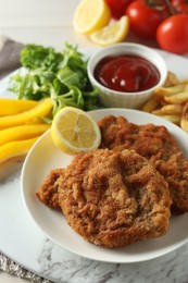 Photo of Tasty schnitzels served with potato fries, ketchup and vegetables on marble board, closeup