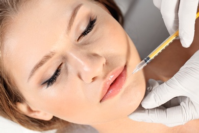 Photo of Young woman getting lips injection in clinic, closeup. Cosmetic surgery