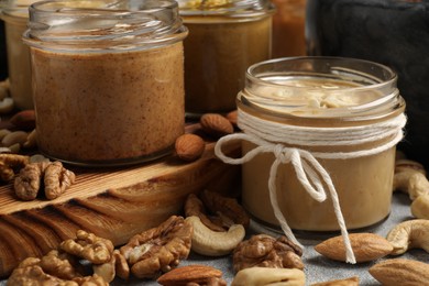 Photo of Tasty nut butters in jars and raw nuts on table, closeup