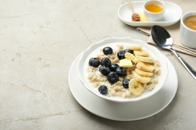 Photo of Tasty oatmeal with banana, blueberries, butter and milk served in bowl on light grey table, space for text