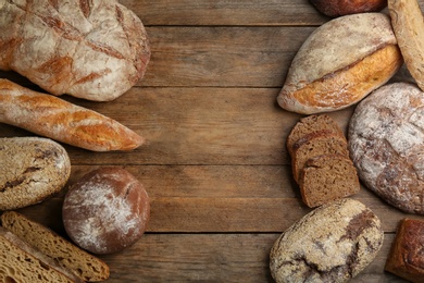 Photo of Different kinds of fresh bread on wooden table, flat lay. Space for text