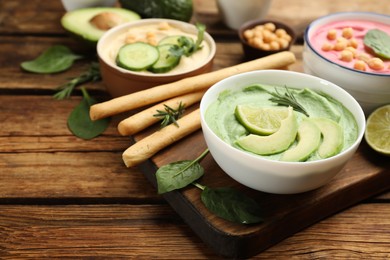 Photo of Bowl of delicious green hummus with rosemary, avocado and lime on wooden table