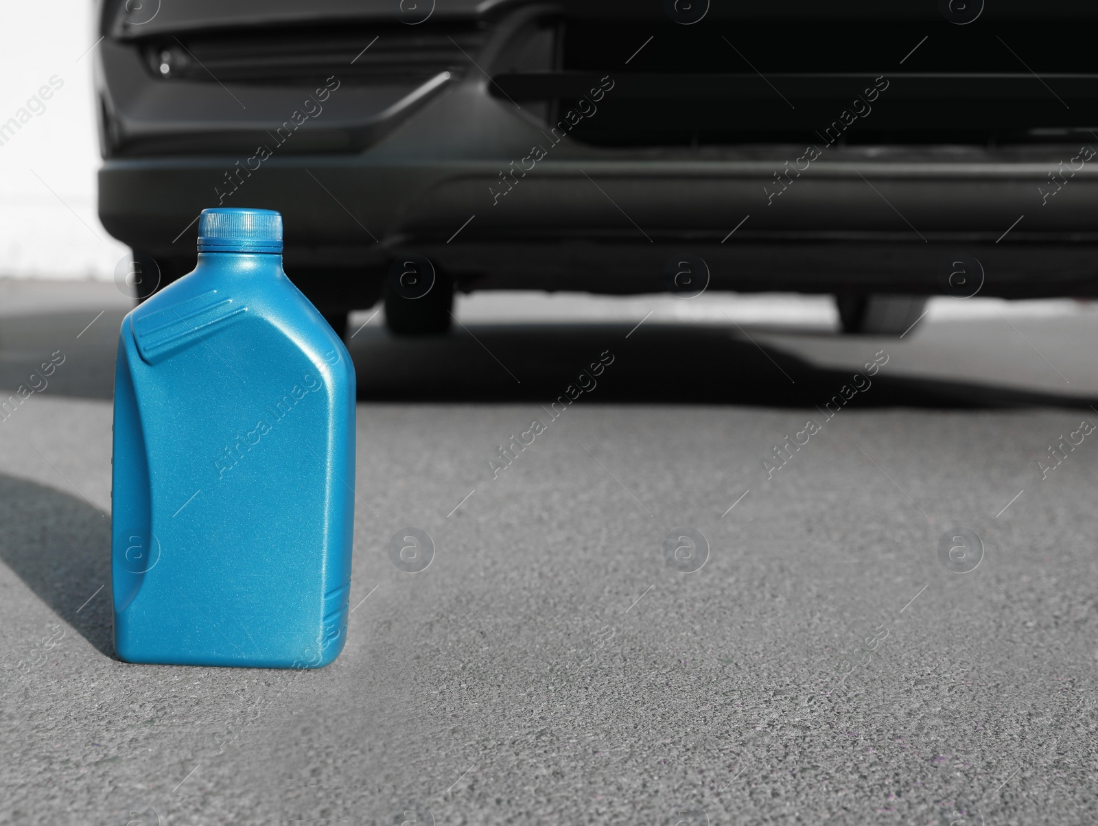 Photo of Blue canister with motor oil near car on asphalt road