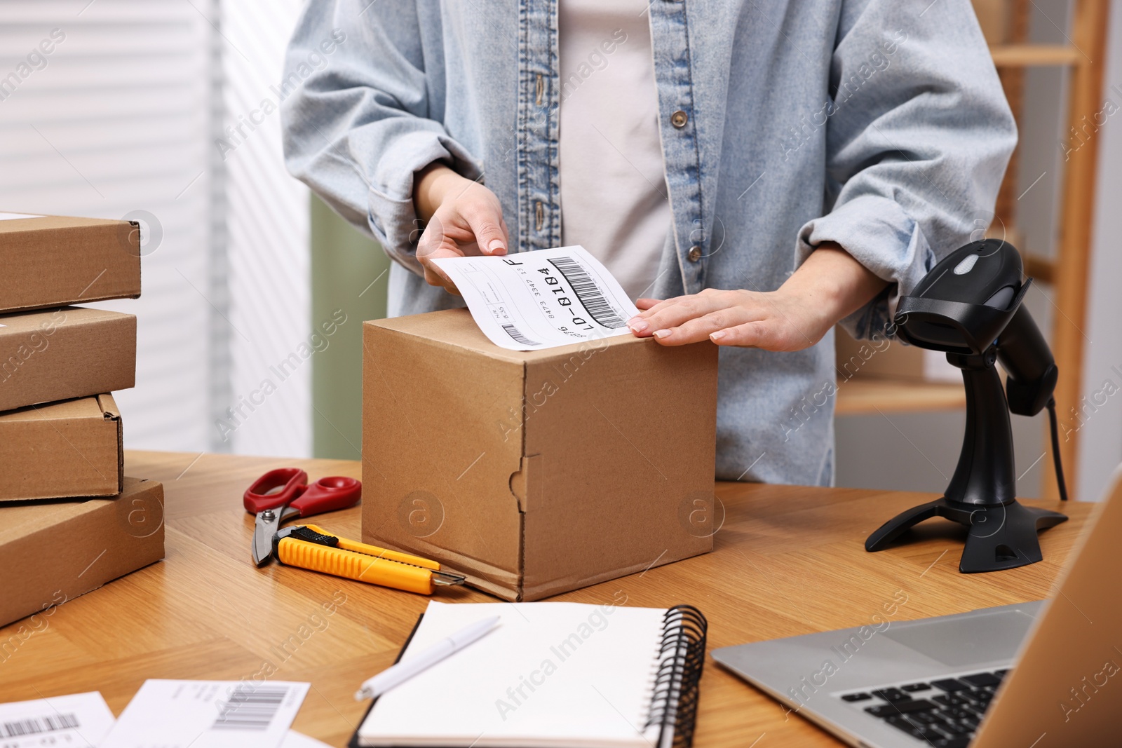 Photo of Parcel packing. Post office worker sticking barcode on box at wooden table indoors, closeup