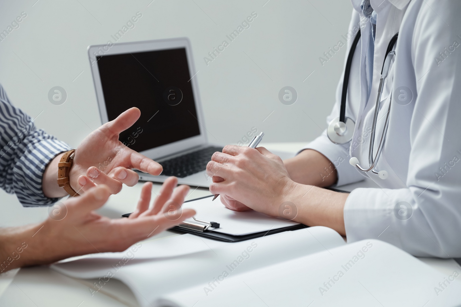 Photo of Doctor consulting patient at white table indoors, closeup