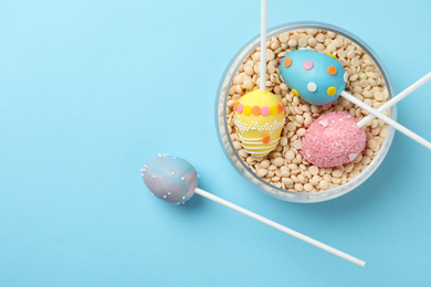 Egg shaped cake pops for Easter celebration on light blue background, flat lay