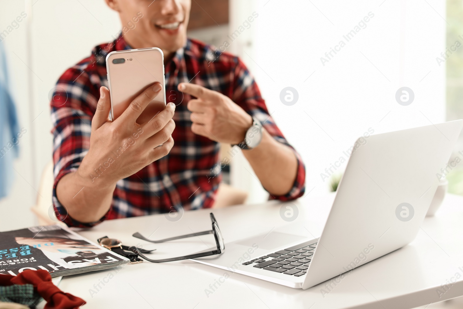 Photo of Tech blogger with laptop and smartphone at table indoors, closeup/ Online broadcast