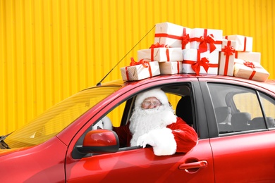 Photo of Authentic Santa Claus driving red car with gift boxes, view from outside