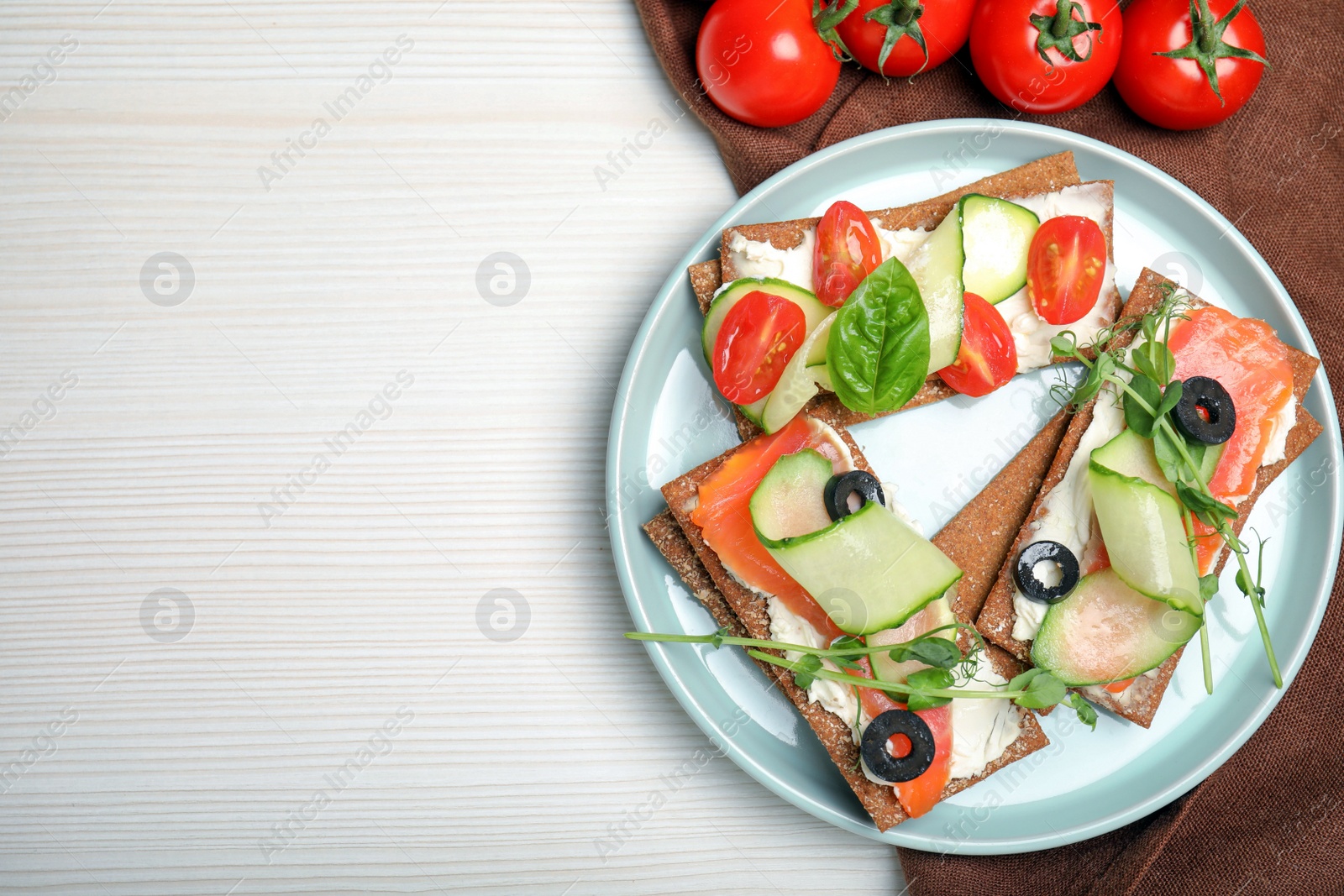 Photo of Tasty rye crispbreads with salmon, cream cheese and vegetables served on white wooden table, flat lay. Space for text